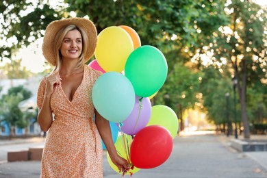 Photo of Smiling woman in hat with bunch of colorful balloons outdoors