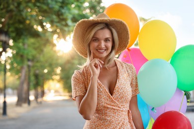 Photo of Portrait of smiling woman in hat with bunch of colorful balloons outdoors