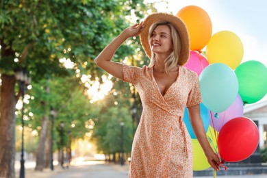 Photo of Smiling woman in hat with bunch of colorful balloons outdoors