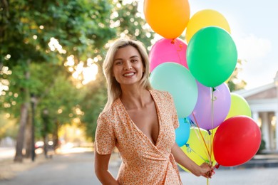 Photo of Portrait of smiling woman with bunch of colorful balloons outdoors