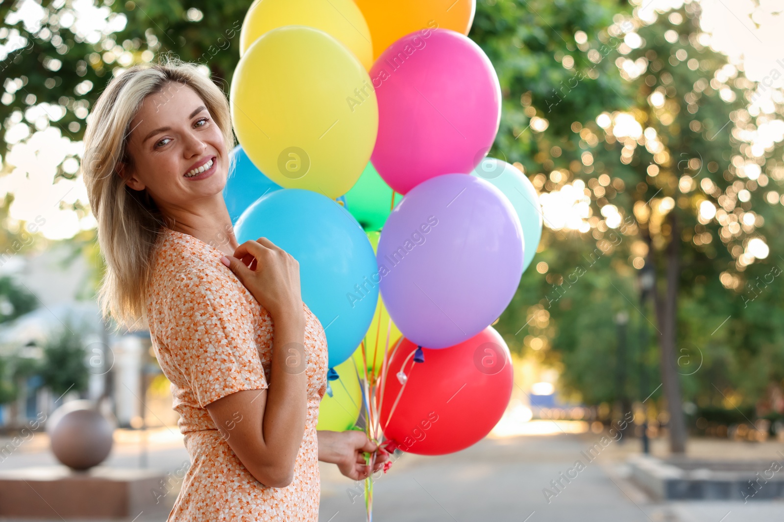 Photo of Portrait of smiling woman with bunch of colorful balloons outdoors