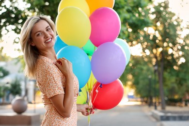Photo of Portrait of smiling woman with bunch of colorful balloons outdoors