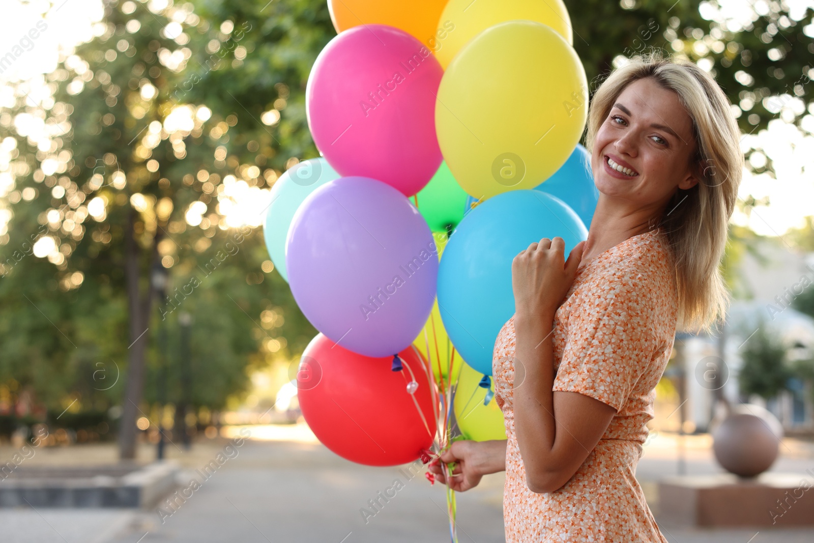 Photo of Portrait of smiling woman with bunch of colorful balloons outdoors