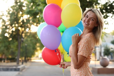Photo of Portrait of smiling woman with bunch of colorful balloons outdoors