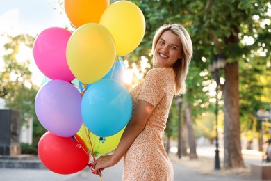 Photo of Portrait of smiling woman with bunch of colorful balloons outdoors