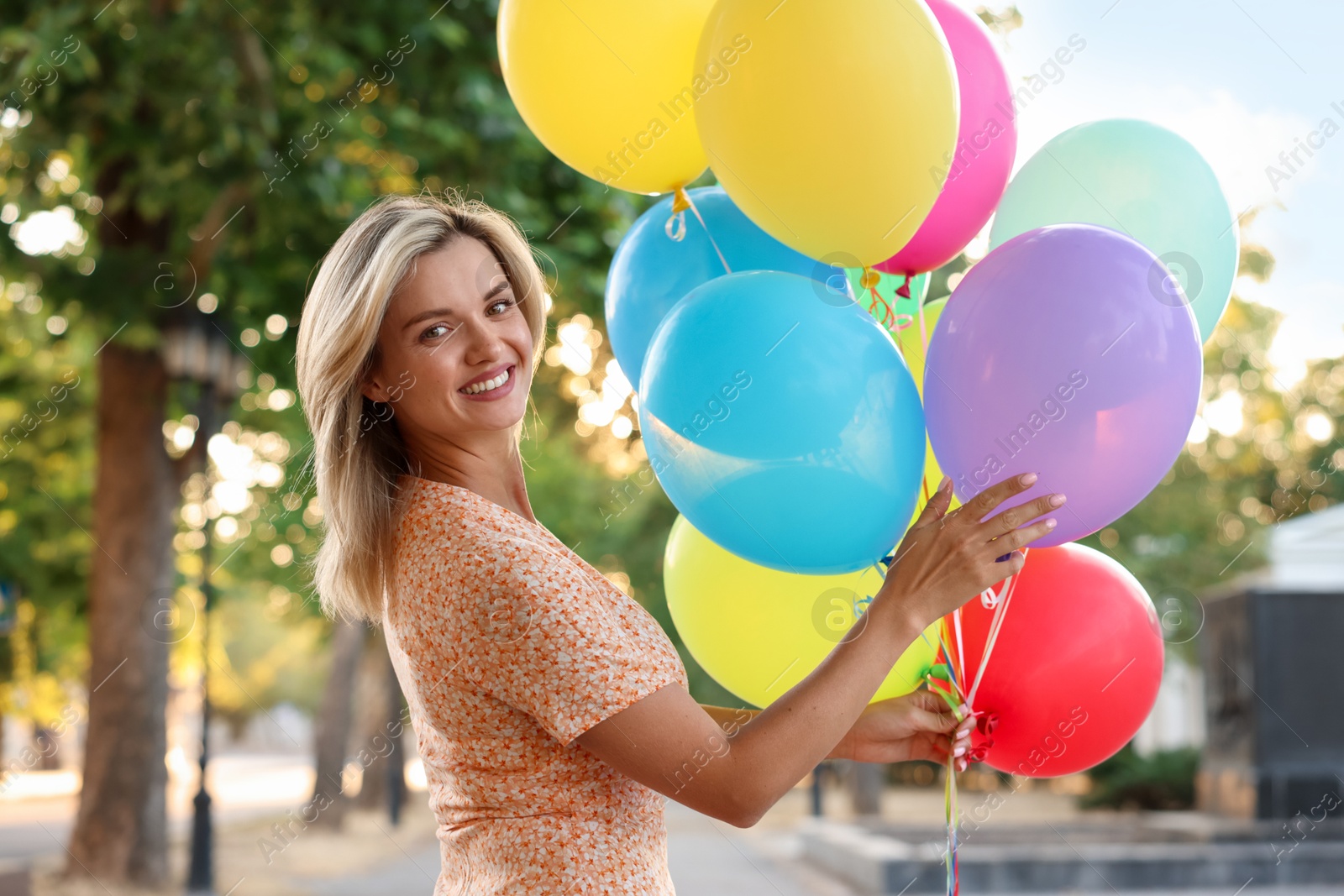 Photo of Portrait of smiling woman with bunch of colorful balloons outdoors