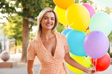 Photo of Portrait of smiling woman with bunch of colorful balloons outdoors