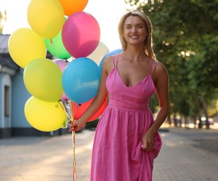 Photo of Smiling woman in dress with bunch of colorful balloons outdoors