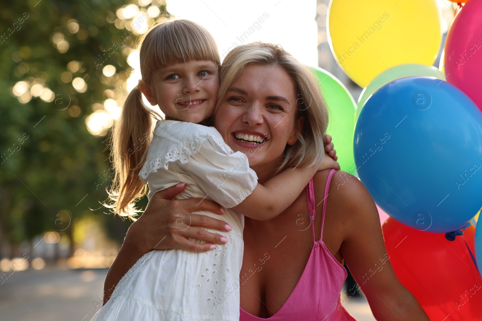 Photo of Family portrait of happy mother with bunch of colorful balloons and her little daughter hugging outdoors