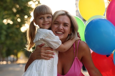 Photo of Family portrait of happy mother with bunch of colorful balloons and her little daughter hugging outdoors