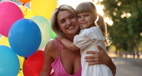 Photo of Family portrait of happy mother with bunch of colorful balloons and her little daughter hugging outdoors