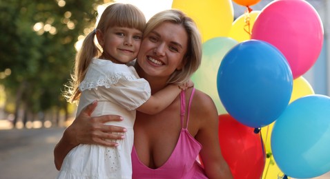 Photo of Family portrait of happy mother with bunch of colorful balloons and her little daughter hugging outdoors