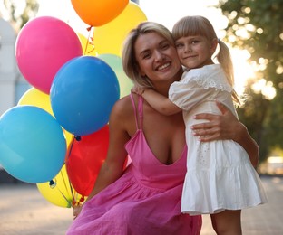 Photo of Family portrait of happy mother with bunch of colorful balloons and her little daughter hugging outdoors