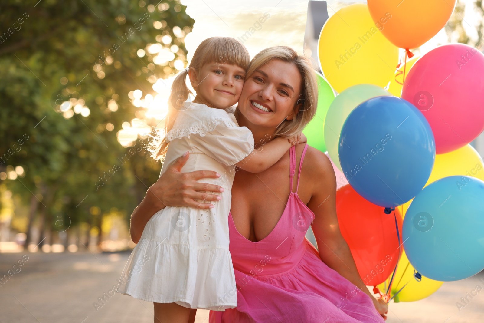 Photo of Family portrait of happy mother with bunch of colorful balloons and her little daughter hugging outdoors