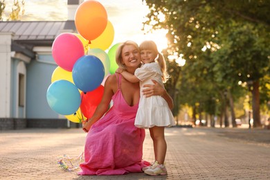 Photo of Happy mother with bunch of colorful balloons and her little daughter hugging outdoors at sunset