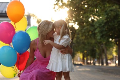 Photo of Happy mother with bunch of colorful balloons and her little daughter hugging outdoors at sunset
