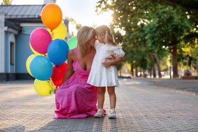 Photo of Happy mother with bunch of colorful balloons and her little daughter hugging outdoors at sunset