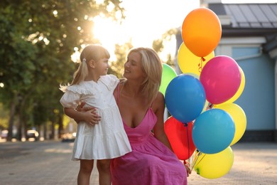 Photo of Happy mother with bunch of colorful balloons and her little daughter hugging outdoors at sunset