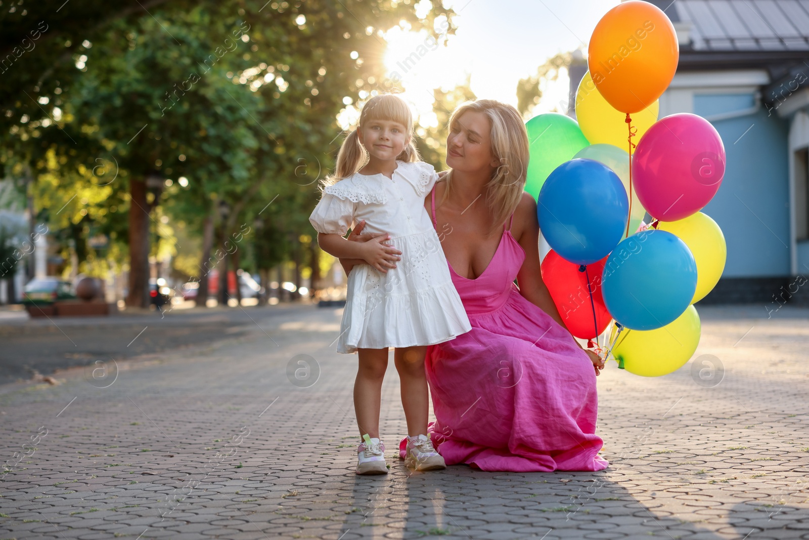Photo of Mother with bunch of colorful balloons and her little daughter hugging outdoors at sunset