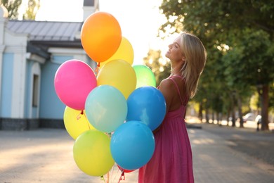 Photo of Smiling woman with bunch of colorful balloons outdoors