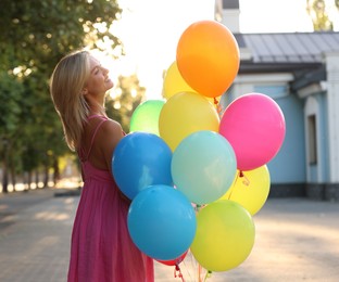 Photo of Smiling woman with bunch of colorful balloons outdoors