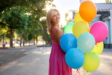 Photo of Smiling woman with bunch of colorful balloons outdoors