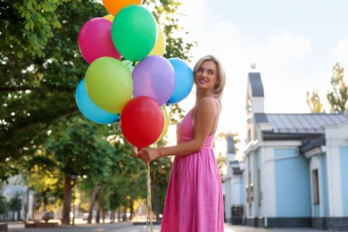 Photo of Smiling woman with bunch of colorful balloons outdoors