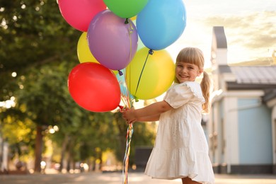 Photo of Portrait of smiling little girl in dress with bunch of colorful balloons outdoors at sunset