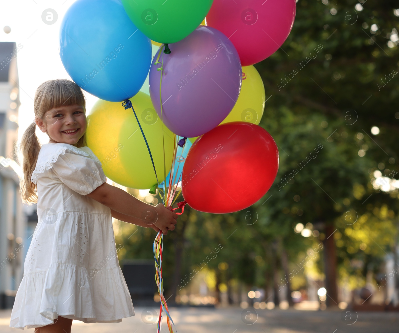 Photo of Smiling little girl in dress with bunch of colorful balloons outdoors