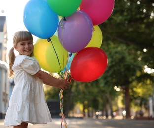 Photo of Smiling little girl in dress with bunch of colorful balloons outdoors