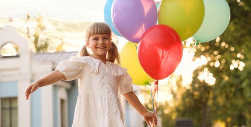 Photo of Smiling little girl in dress with bunch of colorful balloons outdoors at sunset
