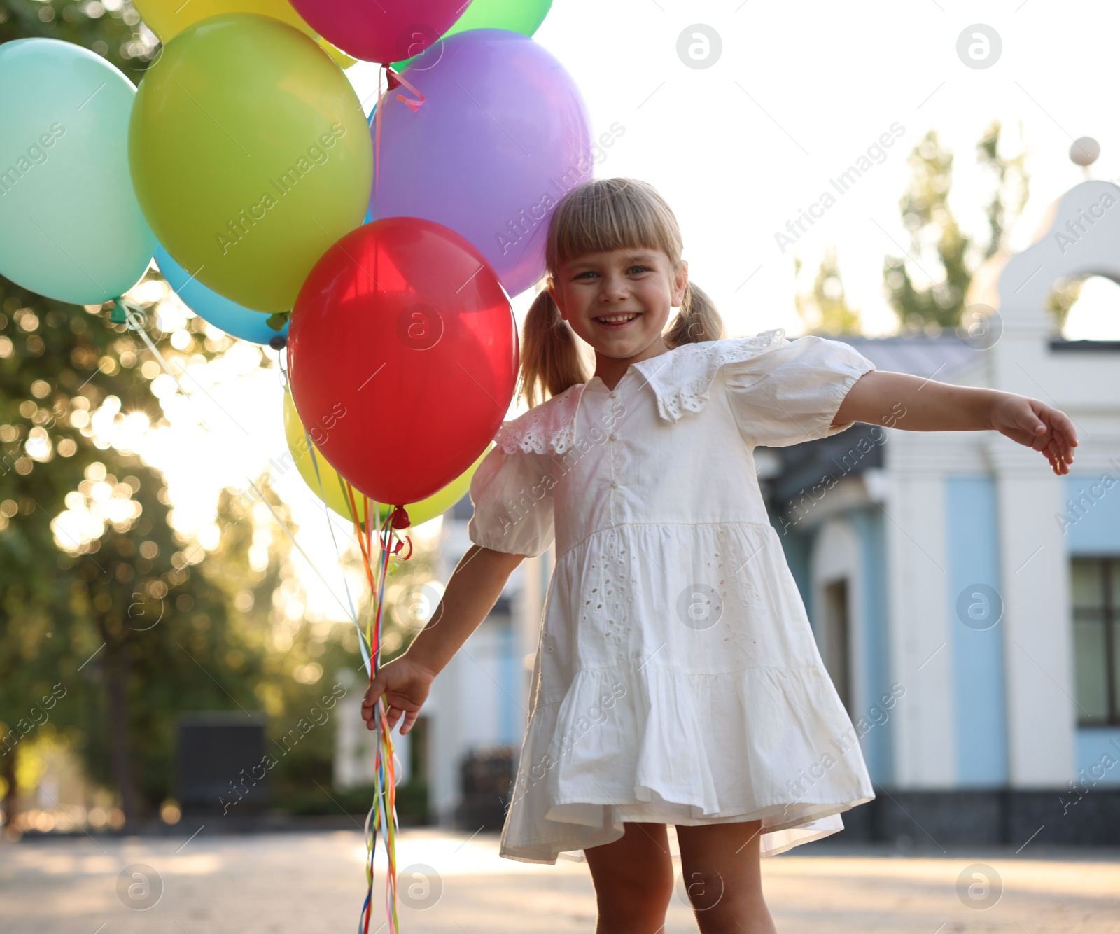 Photo of Smiling little girl in dress with bunch of colorful balloons outdoors at sunset