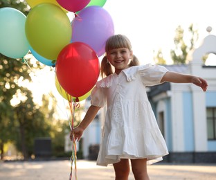 Photo of Smiling little girl in dress with bunch of colorful balloons outdoors at sunset