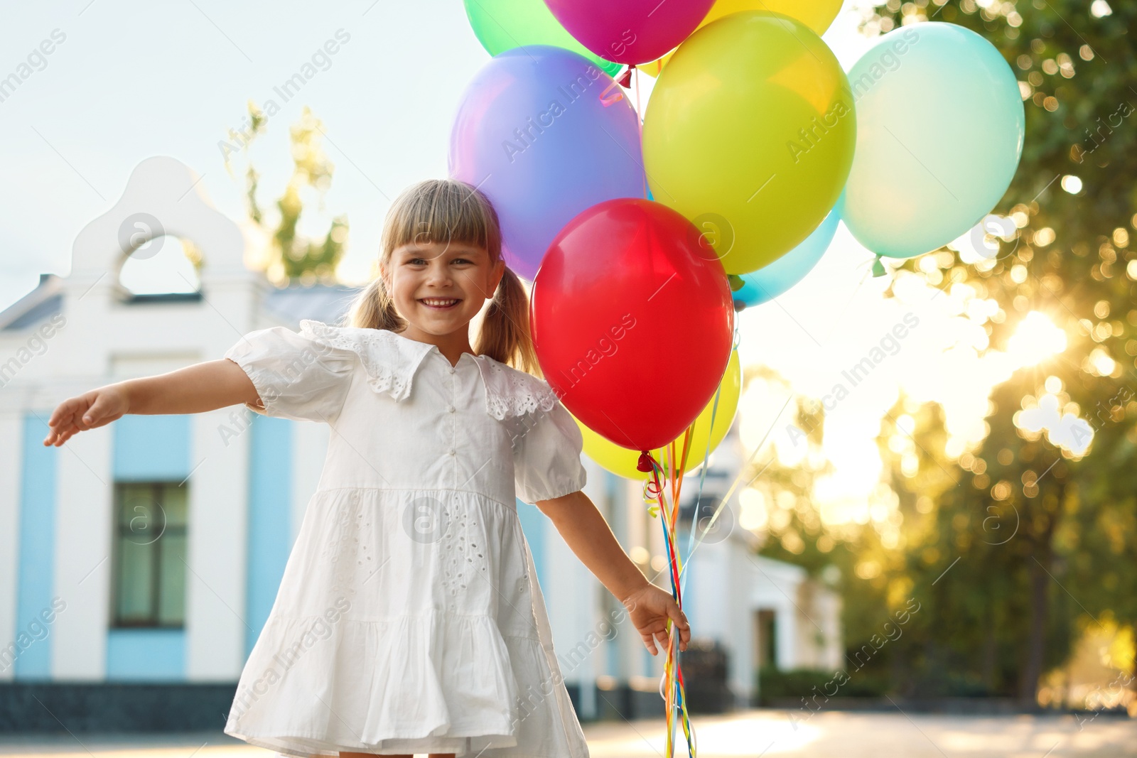 Photo of Smiling little girl in dress with bunch of colorful balloons outdoors at sunset