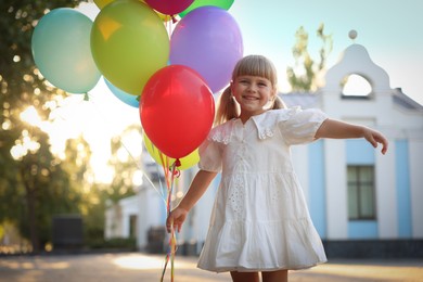 Photo of Smiling little girl in dress with bunch of colorful balloons outdoors at sunset