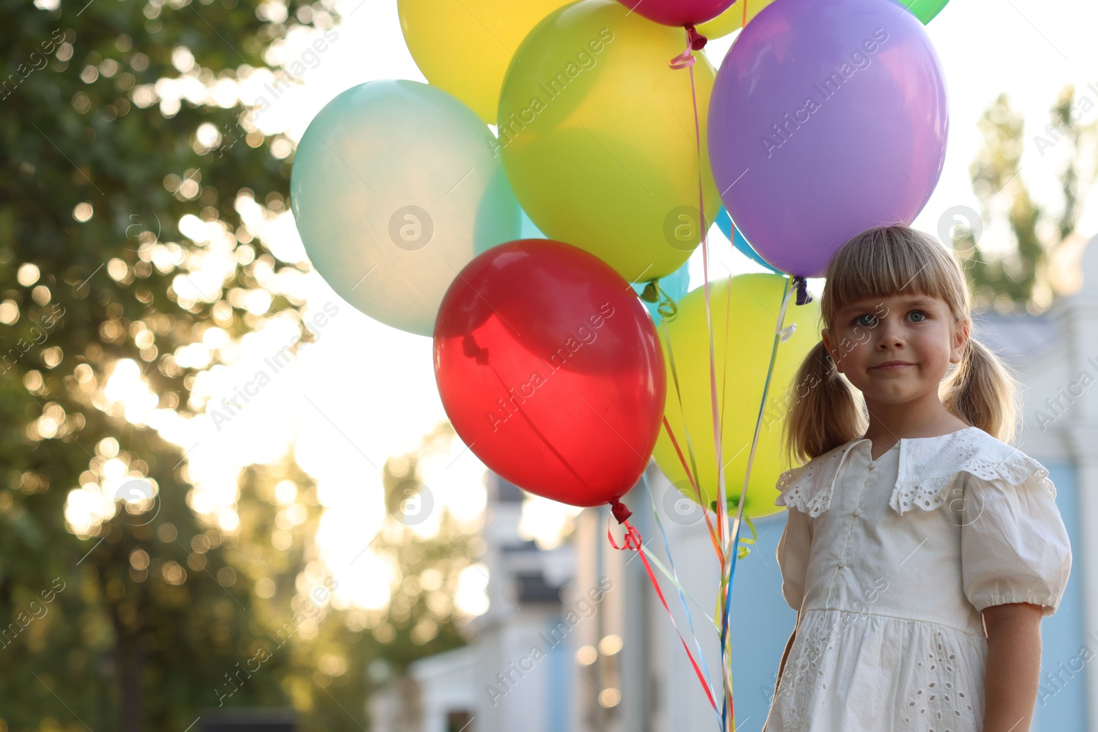 Photo of Cute little girl in dress with bunch of colorful balloons outdoors at sunset