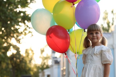 Photo of Cute little girl in dress with bunch of colorful balloons outdoors at sunset