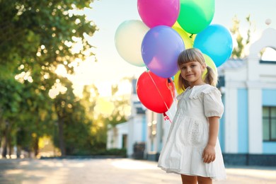 Photo of Cute little girl in dress with bunch of colorful balloons outdoors at sunset. Space for text