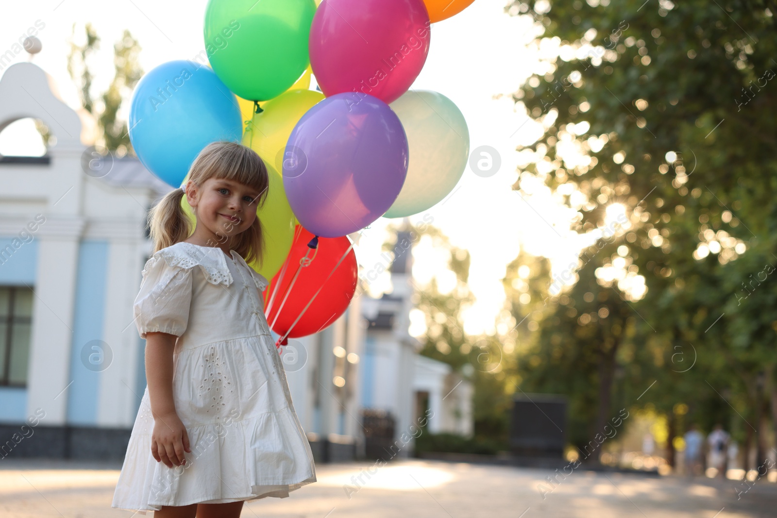 Photo of Cute little girl in dress with bunch of colorful balloons outdoors at sunset. Space for text