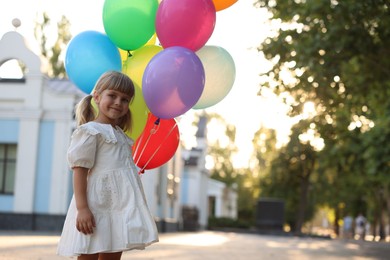 Photo of Cute little girl in dress with bunch of colorful balloons outdoors at sunset. Space for text
