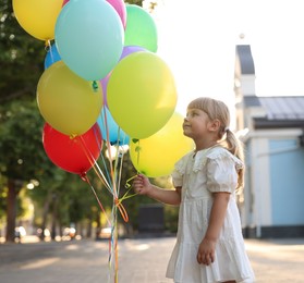 Photo of Cute little girl in dress with bunch of colorful balloons outdoors at sunset