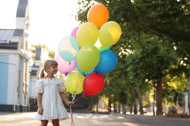 Photo of Cute little girl in dress with bunch of colorful balloons outdoors at sunset