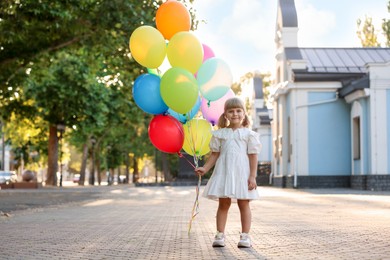 Photo of Cute little girl in dress with bunch of colorful balloons outdoors at sunset