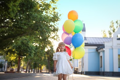Photo of Cute little girl in dress and bunch of colorful balloons outdoors