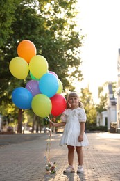 Photo of Cute little girl in dress with bunch of colorful balloons outdoors at sunset