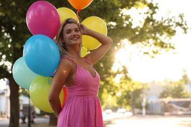 Photo of Smiling woman in dress with bunch of colorful balloons outdoors at sunset