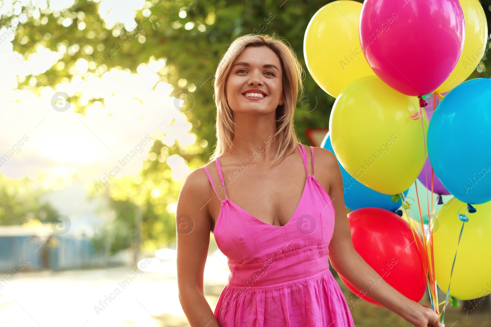 Photo of Smiling woman in dress with bunch of colorful balloons outdoors at sunset
