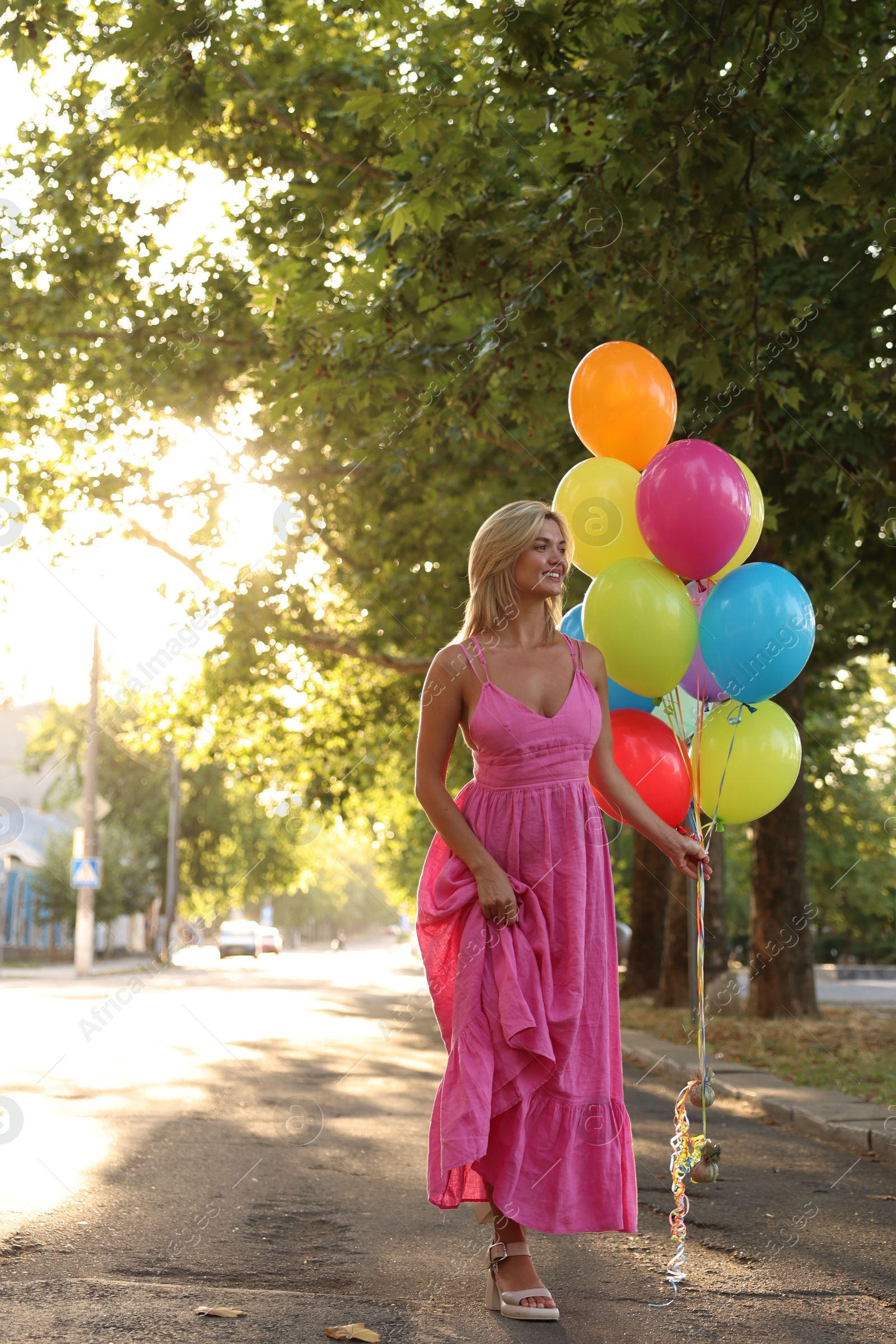 Photo of Smiling woman in dress with bunch of colorful balloons outdoors at sunset