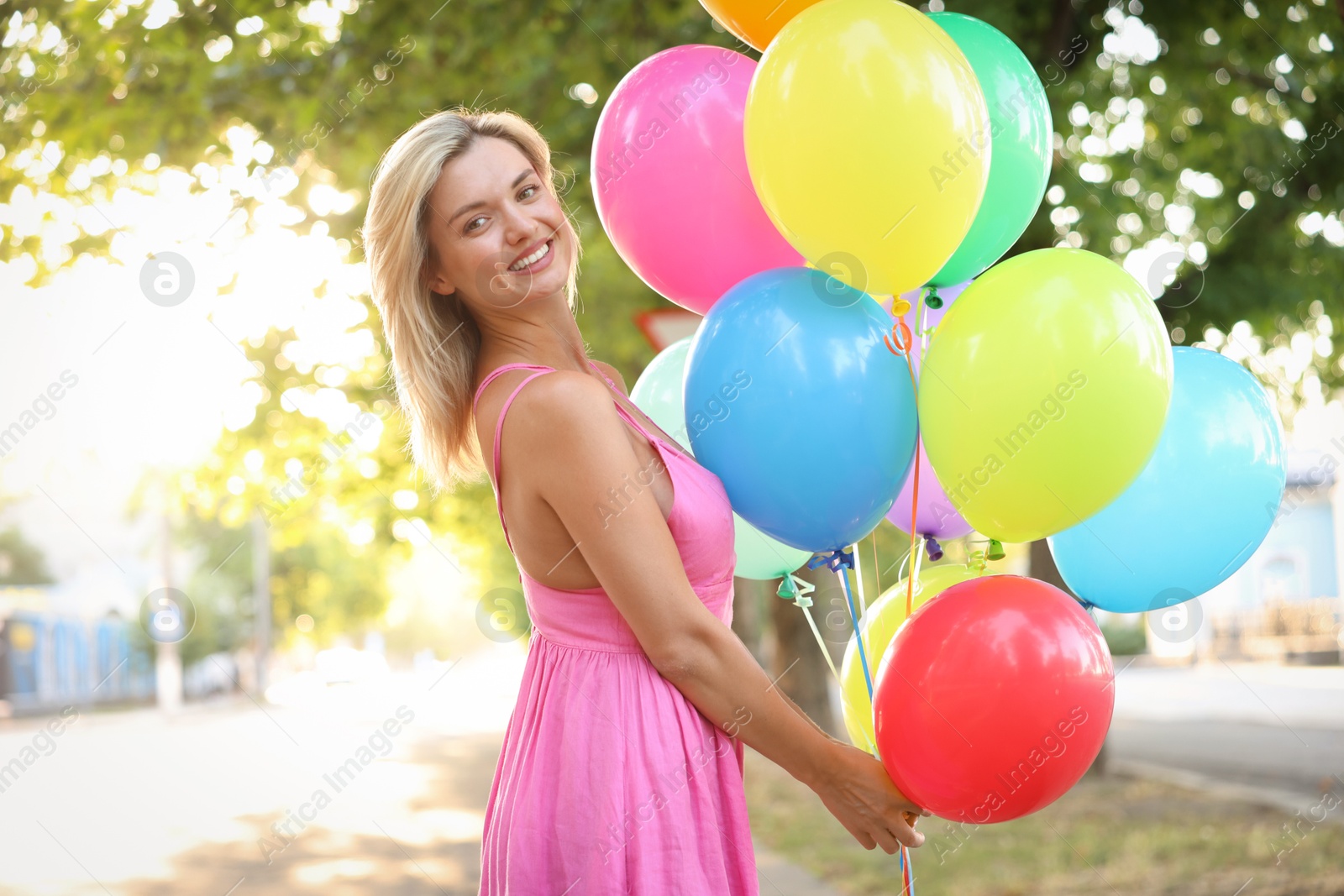 Photo of Portrait of smiling woman in dress with bunch of colorful balloons outdoors