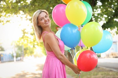 Photo of Portrait of smiling woman in dress with bunch of colorful balloons outdoors